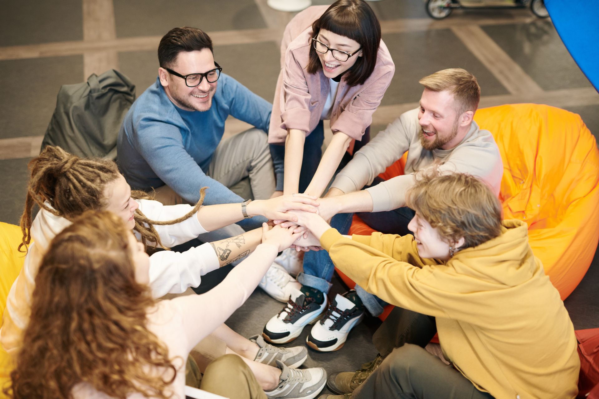 A diverse group sitting in a circle, smiling and stacking their hands together during a group session